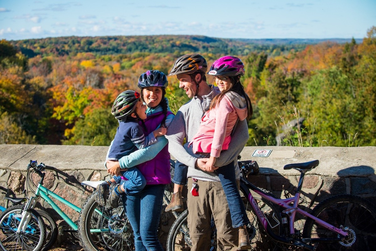 Family of four standing by a rock ledge holding eachother while beside their bikes