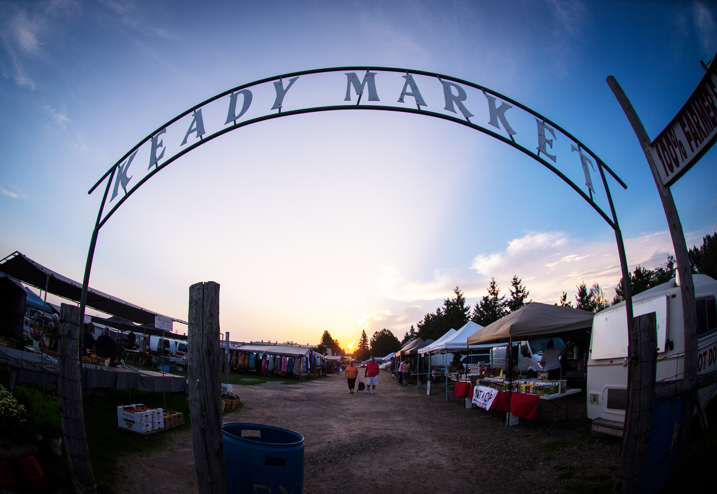 Entrance arch to an outdoor market at sunset, with vendor tents on both sides.