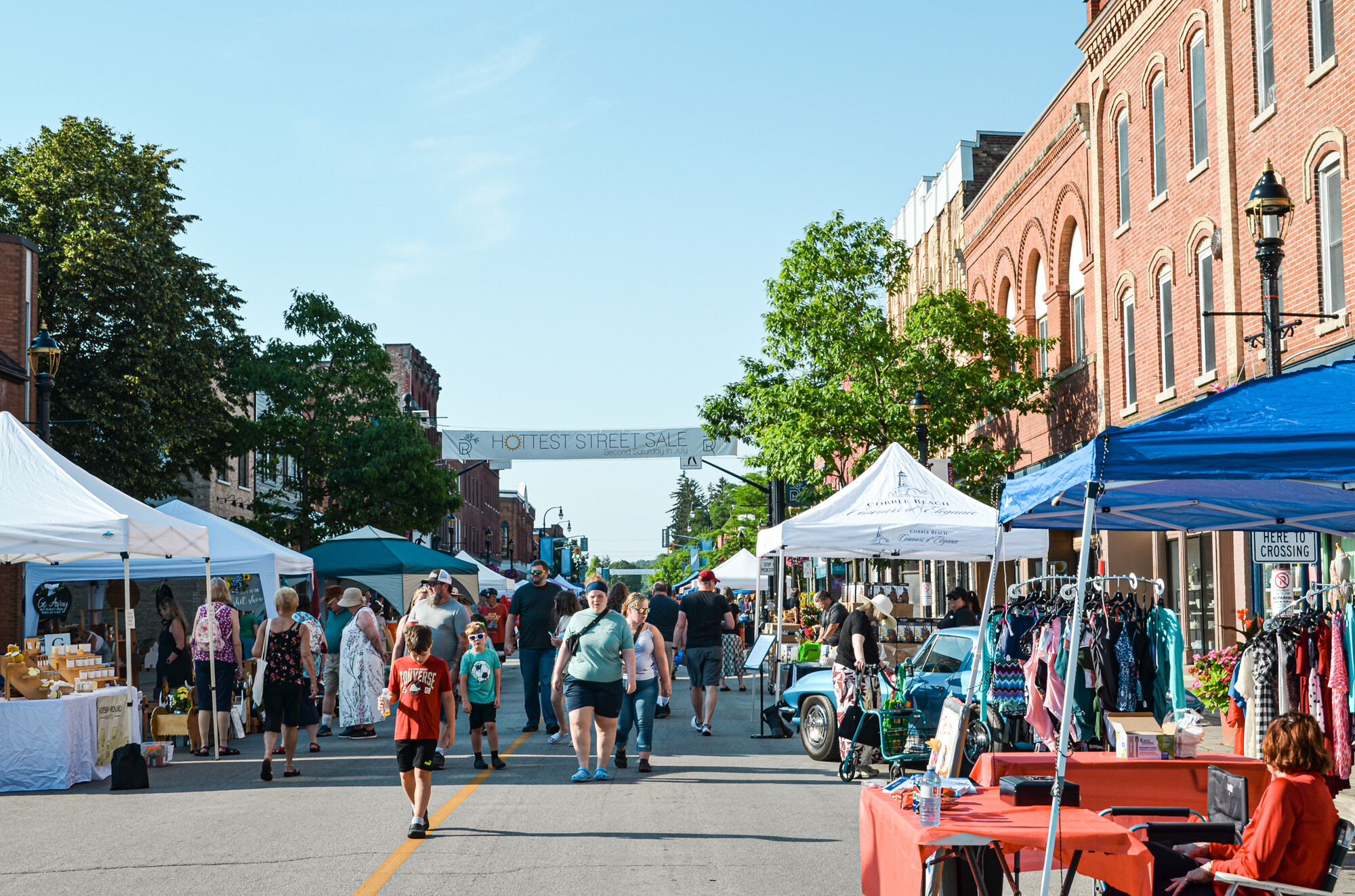 An outdoor street sale. Tented stalls and walking customers on a city street.