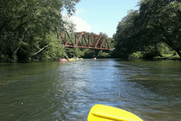 someone paddling on river with bridge in background