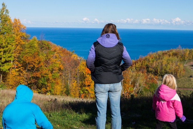 a woman and two kids looking out at a view of autumn leaves