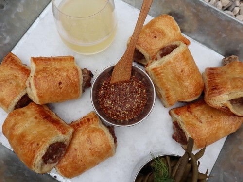 Goldenly baked sausage rolls with a small metal ramekin of dijon mustard