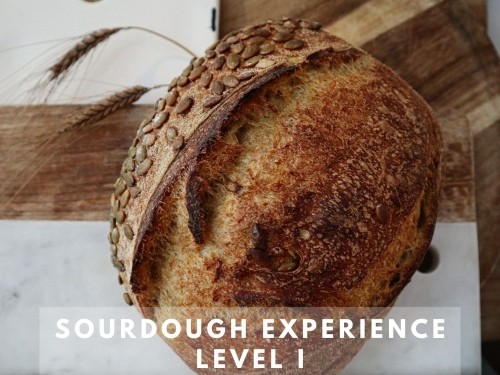 A loaf of bread with pumpkin seeds on the outside, propped up against wood and marble cutting boards
