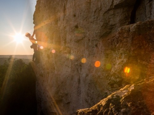 A person climbing up a vertical cliff with the sun shining in the background