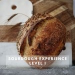 A loaf of bread with pumpkin seeds on the outside, propped up against wood and marble cutting boards