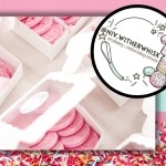 Boxes of bright pink macarons arranged neatly on a light surface. A circular logo on the right shows baking illustrations and text: “@Niv.WitherWhisk – microbakery + creative baking instructor.” Bottom border features colorful sprinkles.