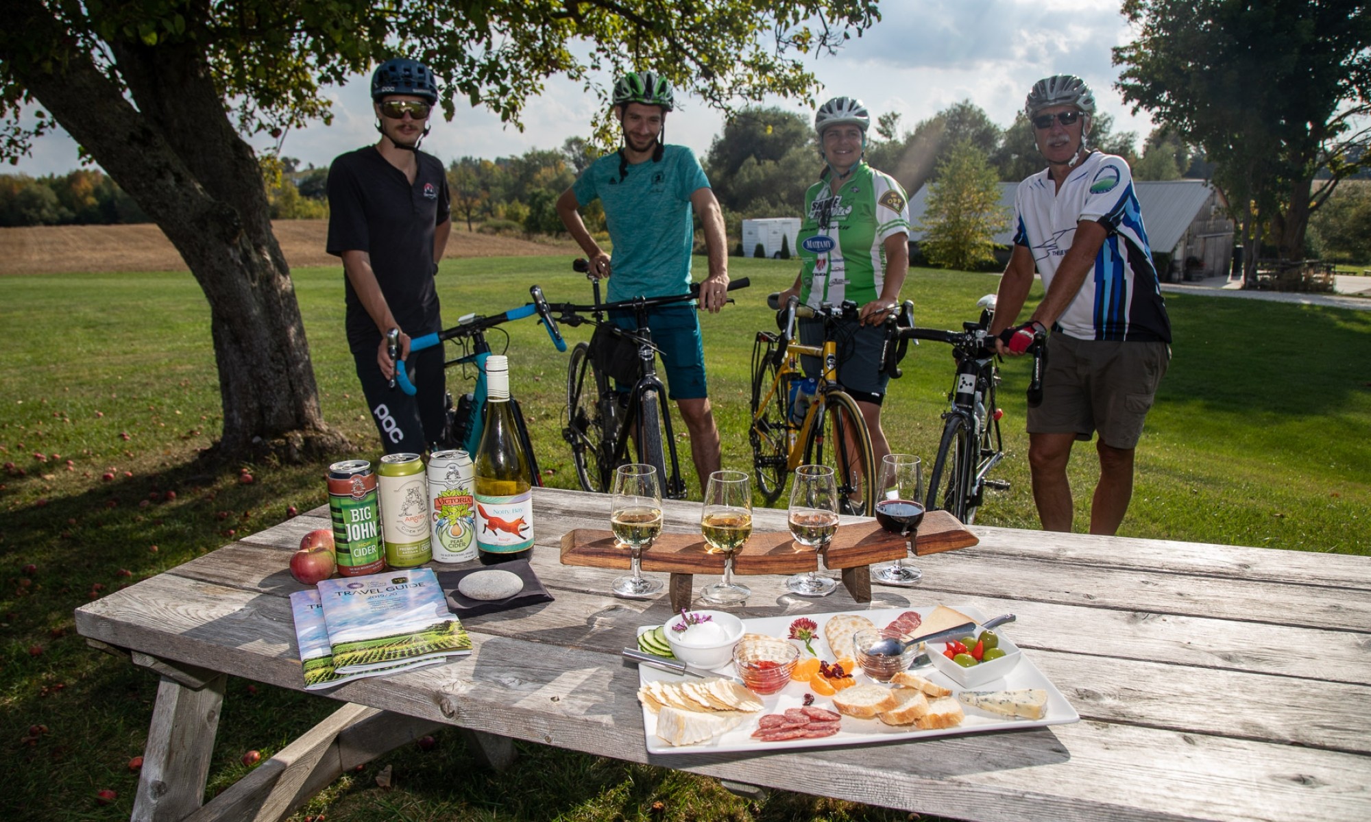Four cyclists standing behind a charcuturie platter and flight of wine